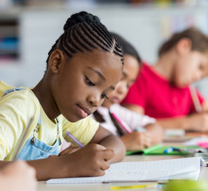 Schülerin schreibt an einem Schreibtisch im Klassenzimmer