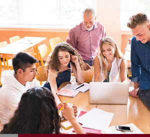 Mehrere Schülerinnen und Schüler arbeiten gemeinsam. Im Hintergrund ist eine Lehrkraft zu sehen. 