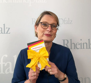 Zu sehen ist Bildungsministerin Dr. Stefanie Hubig. Sie hält ein mit Schleife umwickeltes Grundgesetz in die Kamera. 