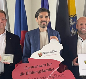 Auf dem Foto von links nach rechts zu sehen sind: Carsten Brock, Ersten Beigeordnete der Gemeinde Haßloch,  Bildungsminister Sven Teuber sowie der Erste Beigeordneter des Kreises Bad Dürkheim, Timo Jordan. Alle drei halten gemeinsam den in den Umrissen des Landes Rheinland-Pfalz gestalteten Förderbescheid in die Kamera. 
